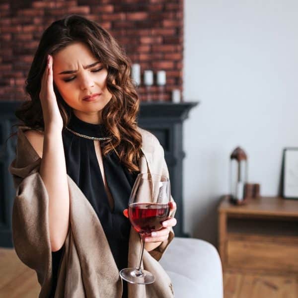 YOUNG WOMAN WITH A HEADACHE HOLDING A GLASS OF RED WINE