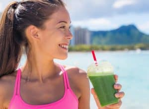 Pretty woman wearing a pink top drinking a green juice on the beach