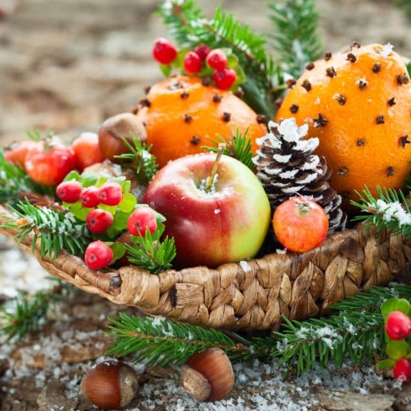 Nutritional tips for winter skin glow: basket with apples, oranges, berries, chestnuts holly leaves beside basket