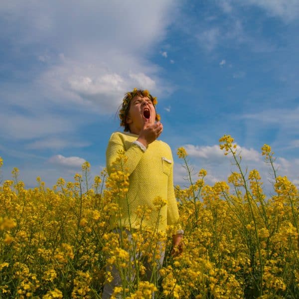 SEASONAL ALLERGY RELIEF THROUGH DIETARY SUPPLEMENTS: PERSON SNEEZING STANDING IN A FIELD OF YELLOW FLOWERS