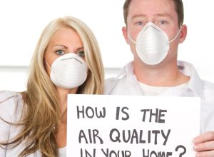 man-and-woman-wearing-masks-holding-sign-saying-how-is-the-air-quality-in-your-home